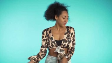 Afro saçlı, güzel Afro-Amerikalı kadın. Stüdyoda mavi arka planda dans edip gülümsüyor. yavaş çekim
