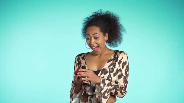 Pretty african-american young woman in leopard print top holding small jewelry box on blue wall background. Girl smiling, she is happy to get present, offer of marriage. — ストック動画