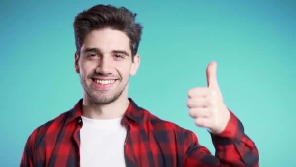 一个积极向上的年轻人对着摄像机笑. 希斯特的家伙用大拇指在蓝色背景上做记号. 赢了 成功。 身体语言. — 图库视频影像
