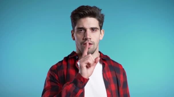 Hombre guapo europeo sosteniendo el dedo en sus labios sobre fondo azul. Gesto de shhh, secreto, silencio . — Vídeos de Stock