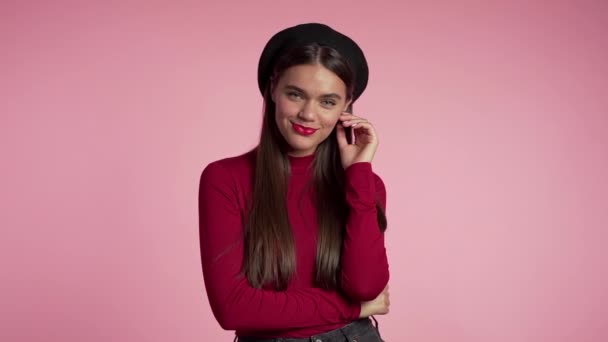 Belle femme européenne joyeuse en tenue rouge et chapeau français souriant à la caméra sur fond de mur rose. Mignon portrait de filles à la mode. Mouvement lent . — Video