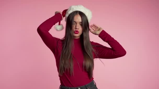 Atrakcyjna dziewczyna w kapeluszu Mikołaja świętuje Boże Narodzenie lub Nowy Rok na różowym tle. Szczęśliwa piękna kobieta uśmiechnięta i dobrze się bawiąca. Zwolniony ruch. — Wideo stockowe