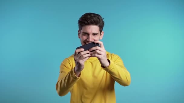 Jóképű férfi játszadozik okostelefonon a kék stúdió falán. Modern technológia - alkalmazások, közösségi hálózatok. Lassú mozgás.. — Stock videók