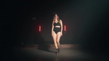 Uzun saçlı, seksi elbiseli güzel bir kadın karanlık odada dans ediyor. Modern dans, yaşam tarzı, yetenekli kız. Yavaş çekim