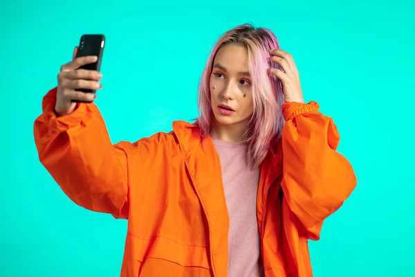 Κορίτσι με ροζ μαλλιά και εξαιρετική εμφάνιση κάνει selfie σε μπλε φόντο. Χρήση σύγχρονης τεχνολογίας - smartphone, κοινωνικά δίκτυα — Φωτογραφία Αρχείου