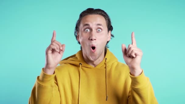 Porträt eines nachdenklichen jungen Mannes in Gelb, der auf blauem Studiohintergrund mit erhobenem Zeigefinger eine Idee hat. Glücklich lächelnder Student zeigt Eureka-Geste. — Stockvideo