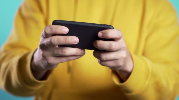 Primeros planos de las manos del hombre jugando juego en el teléfono inteligente en la pared del estudio azul. Uso de la tecnología moderna - aplicaciones, redes sociales. Movimiento lento — Vídeo de stock