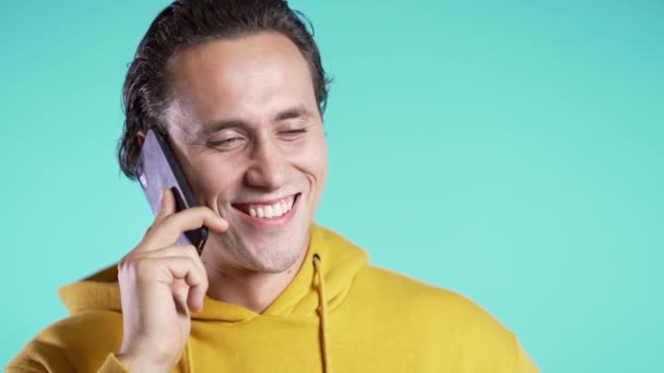 Young man in yellow wear talking on mobile phone on blue background. Copy space. Trendy guy have conversation. Smartphone, technology concept. — Stock Video