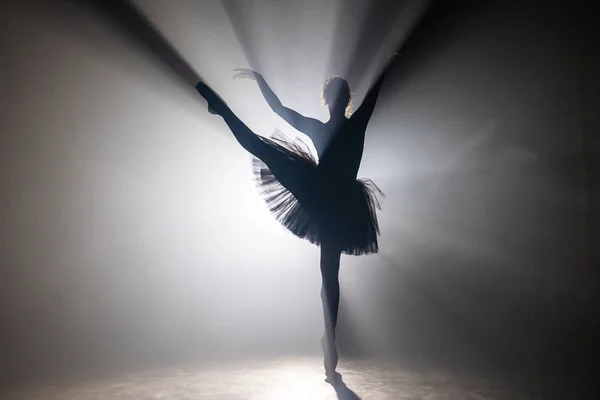 Ballerina professionista danza balletto sotto i riflettori fumo sul grande palco. Bella ragazza che indossa abito tutù nero su sfondo proiettori. Bianco e nero . — Foto Stock