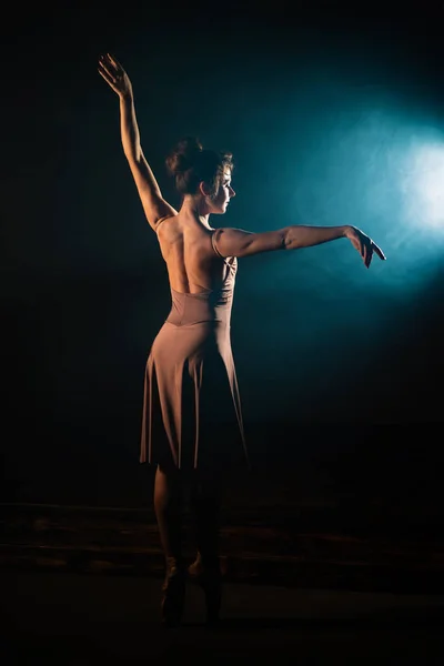 Ballerina oefent haar bewegingen op het donkere toneel. Jong meisje dansend in beige jurk, ronddraaiend en lachend. Genade en tederheid in elke beweging. — Stockfoto