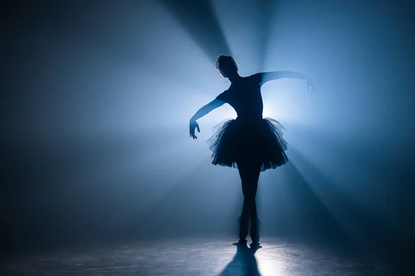 Bailarina de vestido preto tutu dançando no palco com luz azul mágica e fumaça. Silhueta de jovem dançarina atraente em sapatos de balé ponteiro realizando no escuro. Espaço de cópia . — Fotografia de Stock