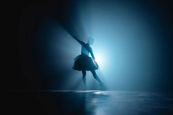 Bailarina de vestido preto tutu dançando no palco com luz azul mágica e fumaça. Silhueta de jovem dançarina atraente em sapatos de balé ponteiro realizando no escuro. Espaço de cópia . — Fotografia de Stock