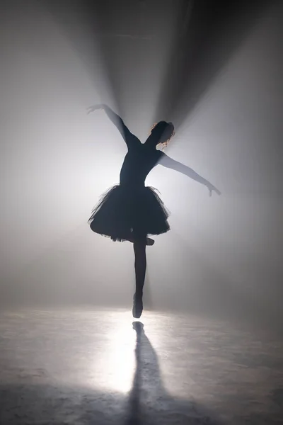 Profesjonalna baletnica tańcząca balet w świetle reflektorów dym na dużej scenie. Piękna młoda dziewczyna w czarnej sukience tutu na tle reflektorów. Czerń i biel. — Zdjęcie stockowe