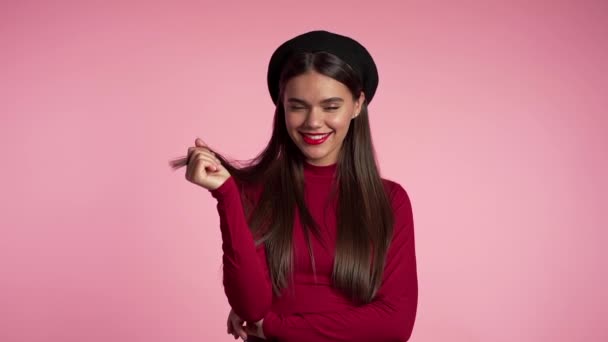 Belle femme européenne joyeuse flirtant en tenue rouge et chapeau français souriant à la caméra sur fond de mur rose. Mignon portrait de filles à la mode. Mouvement lent . — Video