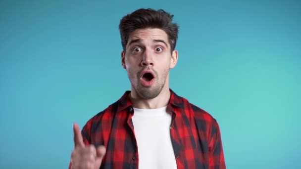 Retrato del joven hombre pensante en rojo teniendo idea momento señalando el dedo hacia arriba en el fondo del estudio azul. Sonriendo feliz estudiante chico mostrando eureka gesto . — Vídeo de stock