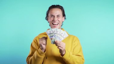 Para gösteren memnun Avrupalı adam mavi duvarda Amerikan doları banknotları. Başarının, kazancının, zaferin sembolü. Yavaş çekim
