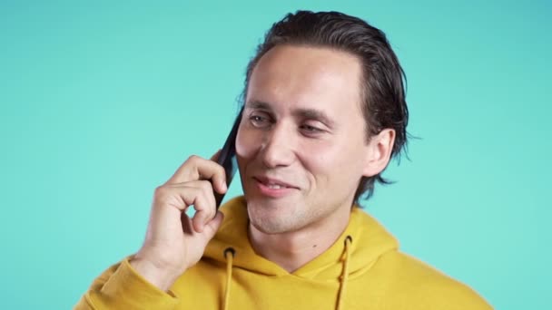 Sarı elbiseli genç adam mavi arka planda cep telefonuyla konuşuyor. Uzayı kopyala Modayı takip eden adam konuşuyor. Akıllı telefon, teknoloji konsepti. — Stok video