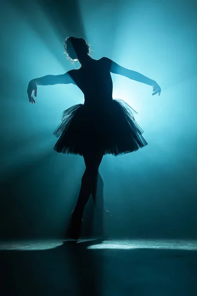 Jonge mooie ballerina op rookpodium dansend modern ballet. Voert gladde bewegingen met de handen tegen schijnwerpers achtergrond. vrouw in zwart tutu kostuum op scène. — Stockfoto