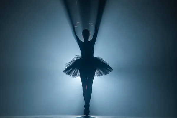 Ballerina in tutù nero si veste danzando sul palco con magica luce blu e fumo. Silhouette di giovane ballerina attraente in ballerine a punta esibendosi nel buio . — Foto Stock
