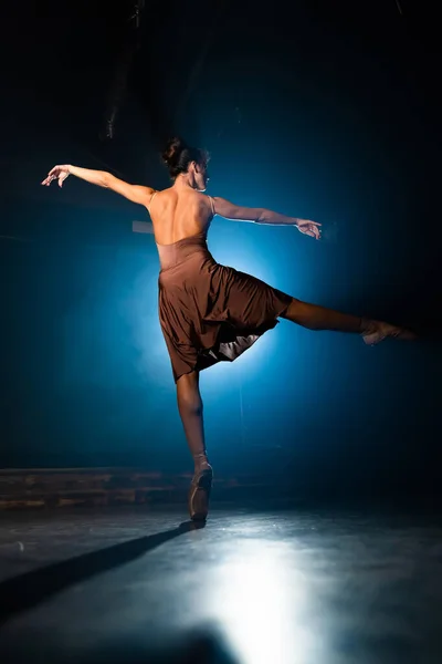 Ballerina oefent haar bewegingen op het donkere toneel. Jong meisje dansend in beige jurk, ronddraaiend en lachend. Genade en tederheid in elke beweging. — Stockfoto