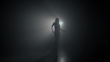 Dumanlı, karanlık arka planda güzel dansçı silueti. Spot ışığı seksi kıza geri yansıyor. Baştan çıkarıcı hareket ediyor..