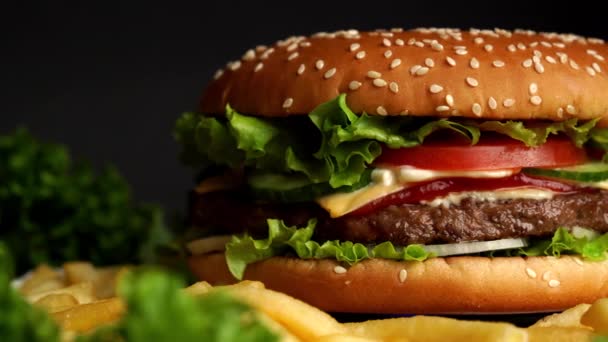 Nagy étvágygerjesztő burger hússal, hagymával, zöldségekkel, olvadt sajttal, salátával és majonézes szósszal. Elszigetelt hamburger forog a sötét füst háttér, közelkép — Stock videók