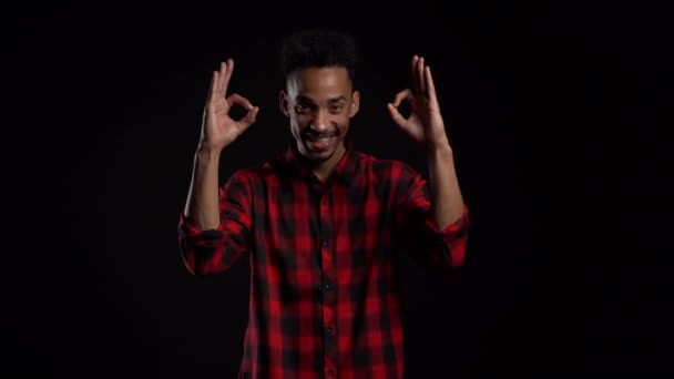 Hombre guapo en ropa roja en negro fondo del estudio sonríe a la cámara y da señal de ok. Feliz chico afroamericano mostrando gesto de aprobación. Ganador. Éxito . — Vídeos de Stock