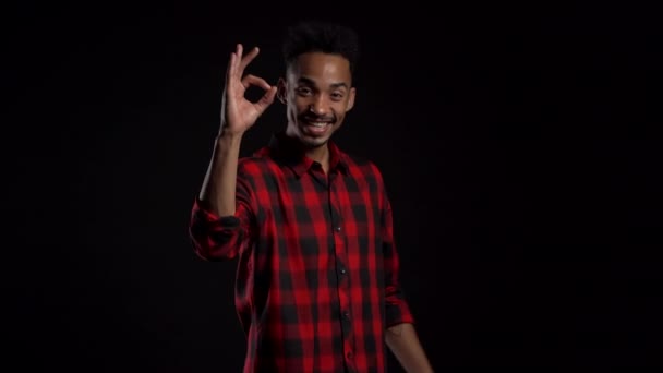 Hombre guapo en ropa roja en negro fondo del estudio sonríe a la cámara y da señal de ok. Feliz chico afroamericano mostrando gesto de aprobación. Ganador. Éxito . — Vídeos de Stock