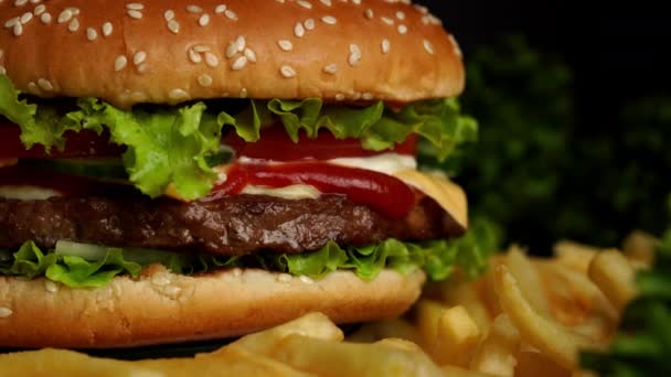 Hamburguesa de carne jugosa con chuleta, cebolla, verduras, queso derretido, lechuga, salsa y semillas de sésamo rematadas. Hamburguesa aislada gira sobre fondo oscuro, vista de cerca — Vídeos de Stock