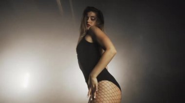 Siyah külotlu çoraplı genç bir kadın karanlık odada müzik eşliğinde dans ediyor. Cinsel dans, koreografi, sanat anlayışı.