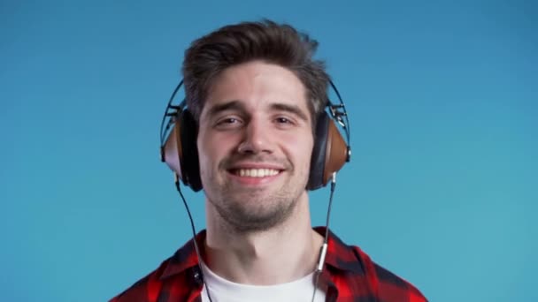 Knappe man met een hoofdtelefoon die danst met een hoofd geïsoleerd op een blauwe achtergrond. Feest, muziek, lifestyle, radio en disco concept. — Stockvideo