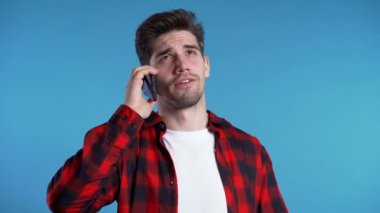 Kırmızılı genç adam mavi arka planda cep telefonuyla konuşuyor. Modayı takip eden adam konuşuyor. Akıllı telefon, teknoloji konsepti.