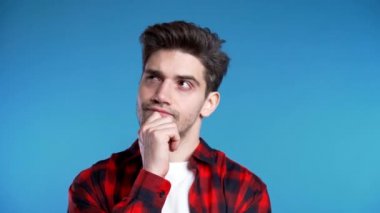 Düşünen adam mavi arka planda etrafa bakıyor. Dalgın yüz ifadeleri için endişelenmiş. Kırmızı gömlekli yakışıklı erkek model..