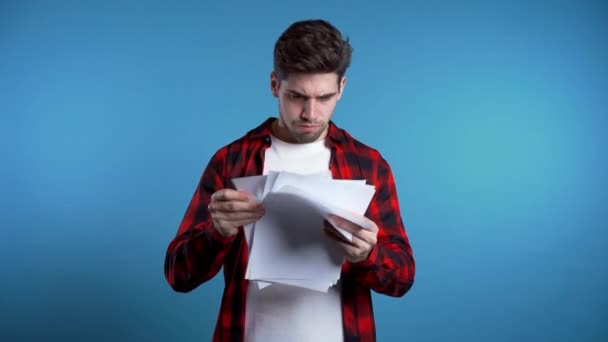 Serious businessman scatters papers on blue background. He is unsatisfied, anxious and confused with work of staff. Young male office employee checks documents, reports. — Stock Video