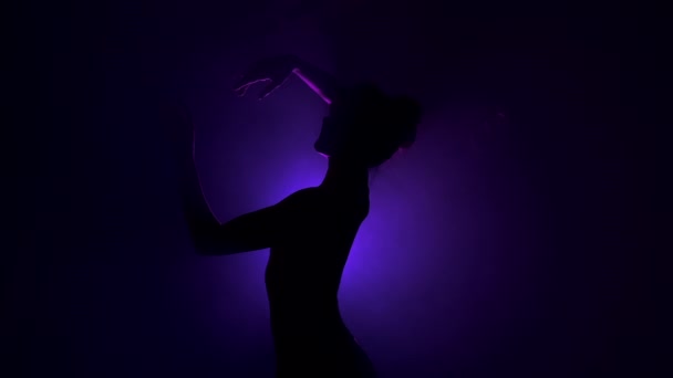 煙のステージ上の若い美しいバレリーナは、現代のバレエを踊る。手で紫色のスポットライトの背景に対して滑らかな動きを実行します。現場で黒いチュチュの衣装の女性。4k — ストック動画