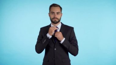 Yakışıklı genç işadamı kravatını düzeltir ve aynadaki gibi kameraya bakar. Mavi stüdyodaki adam. Zarif takım elbiseli şirket üyesi kravatını düzeltiyor. 4k