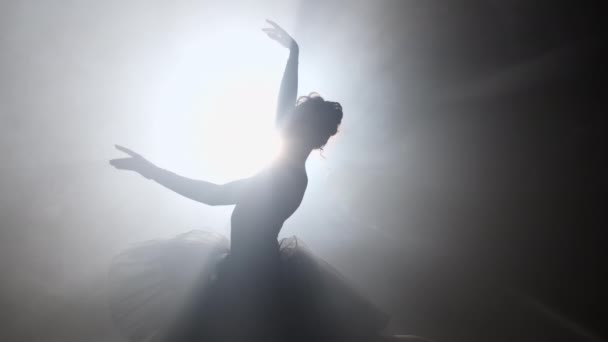 Solo performance door ballerina in tutu jurk tegen de achtergrond van lichtgevende neon schijnwerpers in het theater. Silhouet van een vrouw in puntschoenen die klassieke bewegingen danst. 4k. — Stockvideo