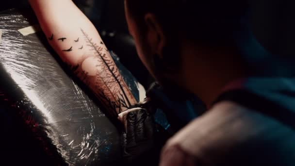 Portret mężczyzny tatuażysty z dredami przedstawiający proces tworzenia tatuażu na ciele kobiety pod lampą. Zwolnij trochę. Profesjonalny artysta pracujący w sterylnych rękawiczkach — Wideo stockowe