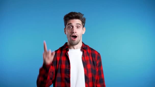 Portrét mladého přemýšlejícího muže v červeném s nápadným okamžikem ukazujícím prstem na pozadí modrého studia. Usmívající se šťastný student chlap ukazující eureka gesto. — Stock video