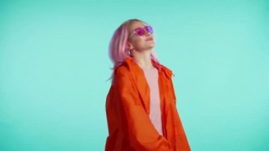 Portakal rengi yağmurluklu genç ve çekici Amerikalı hippi kadın hayatın tadını çıkarıyor ve mavi arka planda dans ediyor. Müzik, yaşam tarzı, modern moda konsepti. 4k
