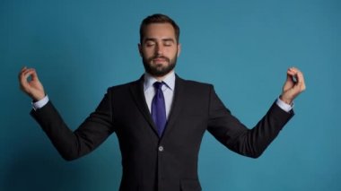 Kampanya kıyafeti içinde sakin bir iş adamı dinleniyor, meditasyon yapıyor. Yakışıklı Avrupalı adam sakinleşiyor, Mudra om ile derin derin nefes alıyor. Ağır çekim. Stüdyo görüntüleri.