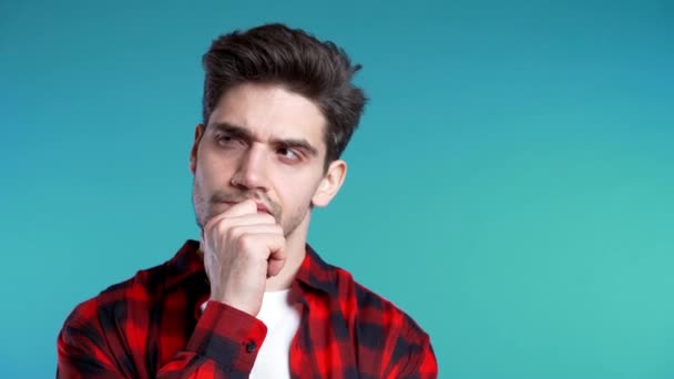 Copiar espacio.Hombre pensante mirando hacia arriba y alrededor sobre fondo azul. Expresiones faciales contemplativas preocupadas. Modelo masculino guapo en camisa roja . — Vídeo de stock