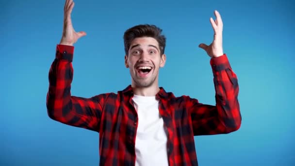 Yes winner gesture. Happy european man rejoices. Handsome guy with stylish hairdo surprised to camera over blue background. — Stock Video