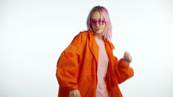 Joven atractiva mujer hipster americana en impermeable naranja disfrutando de la vida y bailando en el fondo blanco. Música, estilo de vida, concepto de moda moderna. 4k — Vídeos de Stock