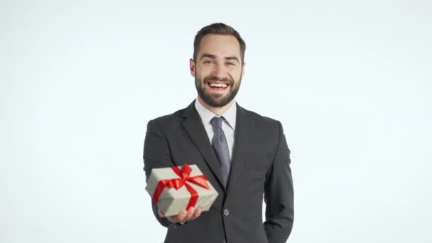 Hombre de negocios guapo en traje da caja de regalo y lo entrega a la cámara. Es feliz, sonriente. Hombre con barba sobre fondo blanco. Imágenes positivas de las vacaciones — Vídeos de Stock