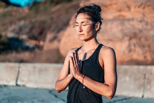 Mulher agradável faz saudação ao sol ao nascer do sol na costa do mar. Mãos no namaste. Yoga, meditação, gratidão, conceito de estilo de vida saudável . — Fotografia de Stock