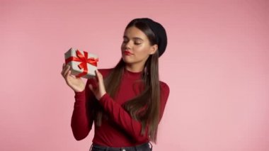 Heyecanlı kadın fiyonklu hediye kutusu aldı. O mutlu ve ilgiyle pohpohlanıyor. Pembe arka planda bugünle dans eden kız. Stüdyo görüntüleri. 4k