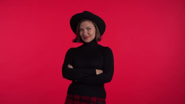 Retrato de jovem bonita mulher no fundo vermelho no estúdio. Menina hipster na moda em chapéu preto e mini-saia xadrez. Senhora sorridente. 4k — Vídeo de Stock