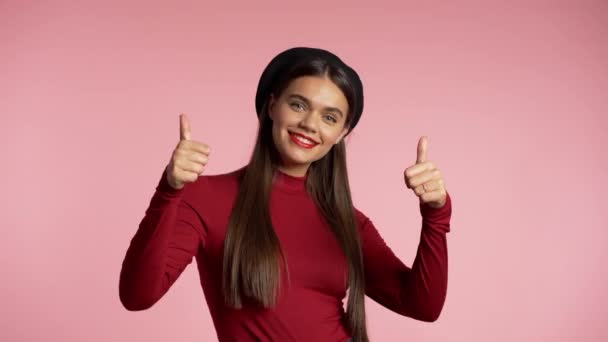 Winner. Success. Positive girl making thumbs up sign over pink background and smiles to camera. Body language. Young hipster woman with perfect red lips make-up and french hat. — ストック動画