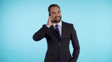 İşadamı mavi arka planda izole edilmiş cep telefonu kullanarak konuşuyor. Resmi takım elbiseli bir iş adamı iş arkadaşıyla memnuniyetle konuşur. Ofis çalışanı, maaşlı işçi, hafta içi konsepti.